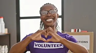 A volunteer is smiling from ear to ear while creating the image of a heart with her hands.