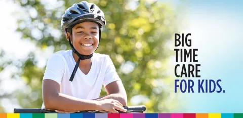 A child on a bike wearing a helmet and smiling at the camera. Text on the picture reads "Big time care for kids."