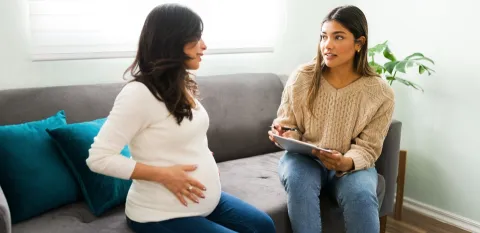 Pregnant woman with a doula sitting on a couch preparing for childbirth.