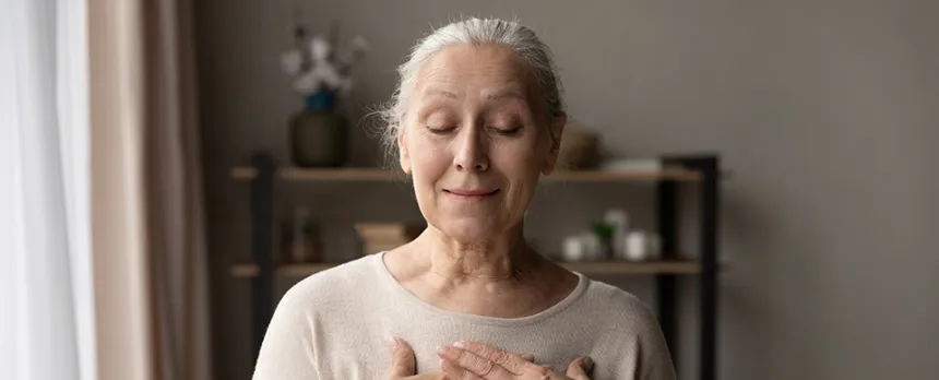 elderly woman mediating with hands over her heart